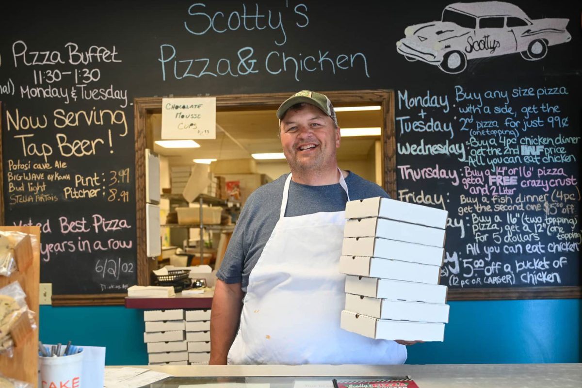Owner at Scotty’s Pizza & Chicken in Marshfield Wisconsin holding pizza boxes at counter